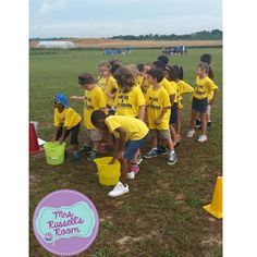 a group of children in yellow shirts are standing around buckets and talking to each other