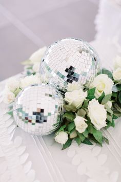 two disco balls sitting on top of a table next to white roses and greenery