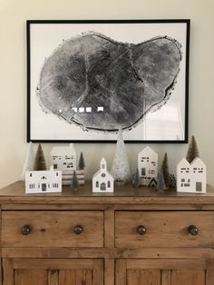 a wooden dresser with white houses and trees on it in front of a framed photograph