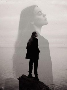 a woman standing on top of a rock next to the ocean with her hair blowing in the wind