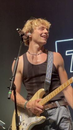 a man with blonde hair playing guitar and singing into a microphone at a music festival