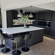 a kitchen with black cabinets and white countertops is pictured in this image, there are four chairs around the island