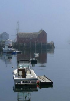 a small boat is docked in the water near some houses and boats on a foggy day