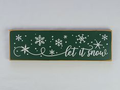 a green sign with white snowflakes and let it snow written in cursive writing