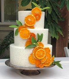 a three tiered white cake with orange slices on top and green leaves around the edges