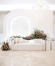 a white couch sitting in front of a chandelier filled with pink flowers and greenery