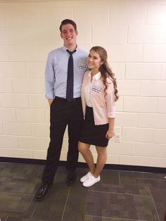 a man and woman standing next to each other in front of a white brick wall