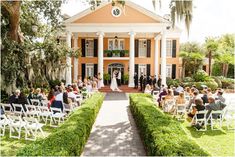 a wedding ceremony in front of an orange house with white chairs and people sitting on the lawn