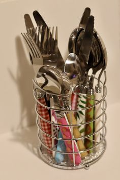 a metal basket filled with forks and spoons on top of a white countertop