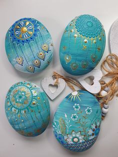 four painted eggs sitting next to each other on top of a white surface with string