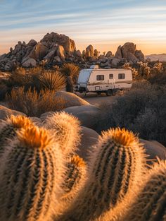 an rv is parked in the desert near rocks and cacti with a sky background