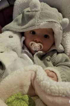 a baby wearing a hat and coat with a pacifier in it's mouth