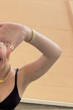 a woman in a black top is smiling and holding her hands up to her head