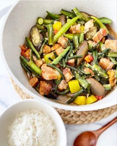 a white bowl filled with stir fried vegetables and rice next to a wooden spoon on top of a table