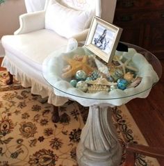 a glass table with seashells and shells on it in front of a white chair