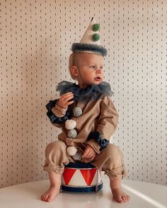 a baby sitting on top of a toy drum wearing a clown hat and holding balls