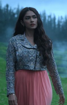 a woman with long hair wearing a dress and standing in front of a tree filled field