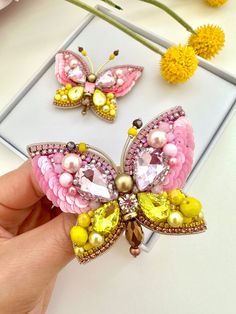 a hand holding a pink and yellow butterfly brooch with pearls on it's wings