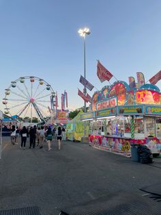 people are walking around an amusement park with carnival rides and ferris wheel in the background