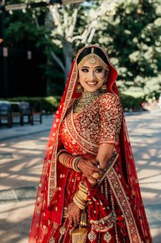 a woman in a red and gold bridal gown posing for the camera with her hands on her hips