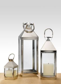 three metal lanterns sitting on top of a wooden table next to each other with one candle in the middle