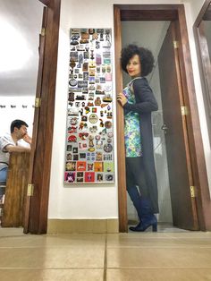 a woman standing in an open doorway next to a wall covered with stickers and magnets