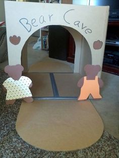 a cardboard bear cave with paper cutouts on the front and sides, sitting on top of a carpeted floor