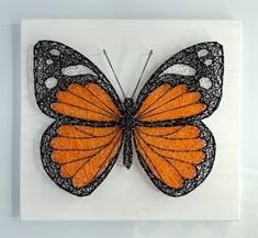 an orange and black butterfly is mounted on a white board with string art in the frame