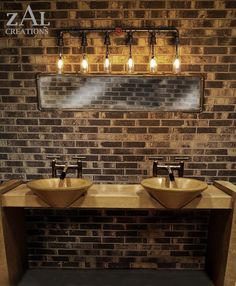 two sinks in front of a brick wall with lights above them and below the mirror