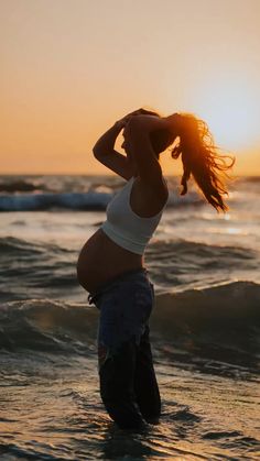 a woman standing in the ocean at sunset with her hands on her head and arms behind her head