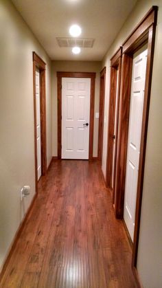 an empty hallway with wooden floors and white door knobs on the left, and wood paneling on the right