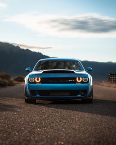 the front end of a blue sports car driving on a road with mountains in the background