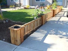 a wooden planter sitting on the side of a road next to a fence and flowers