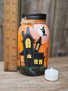 an orange jar with a black house painted on it next to a ruler and candle