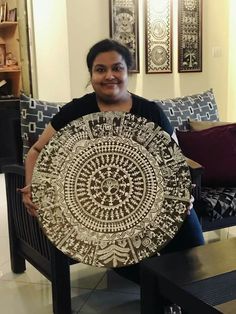 a woman sitting on a couch holding up a plate with an intricate design on it