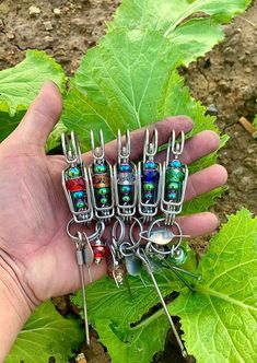 a hand is holding several different sized pins and needles in front of some green leafy plants