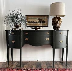 a black dresser with two drawers and a lamp on it next to a framed painting