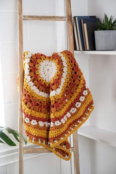 a crocheted blanket draped on top of a ladder next to a potted plant