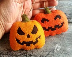 two handmade pumpkins are being held by someone's hand on a wooden table