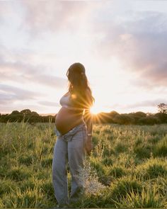 a pregnant woman standing in a field at sunset