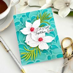 a close up of a card on a table with scissors and flowers in the background