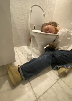 a person sitting on the floor in front of a toilet with its lid up and their head resting on the seat