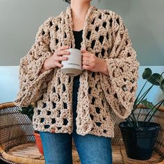 a woman is holding a coffee cup and wearing a crocheted cardigan