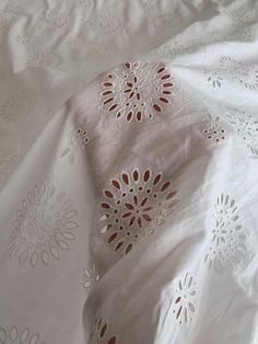 an embroidered white sheet with red and white flowers on it's edges, laying on a bed