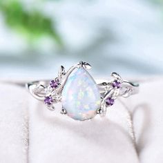 an opal and amethorate ring sitting on top of a white cloth