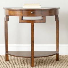 a wooden table with a book on top and a rug underneath it in front of a white wall