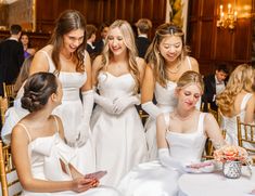 a group of women in white dresses standing around a table