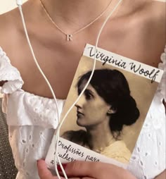 a woman is holding a card with the name virginia woff on it and ear buds in her hand