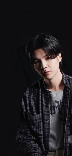 a young man in a black and white shirt is looking at his cell phone while standing against a dark background