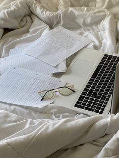 an open laptop computer sitting on top of a bed covered in white sheets and blankets